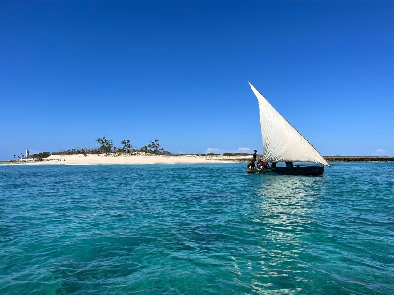 A dhow under full sail off a white sandbank, on turquoise water