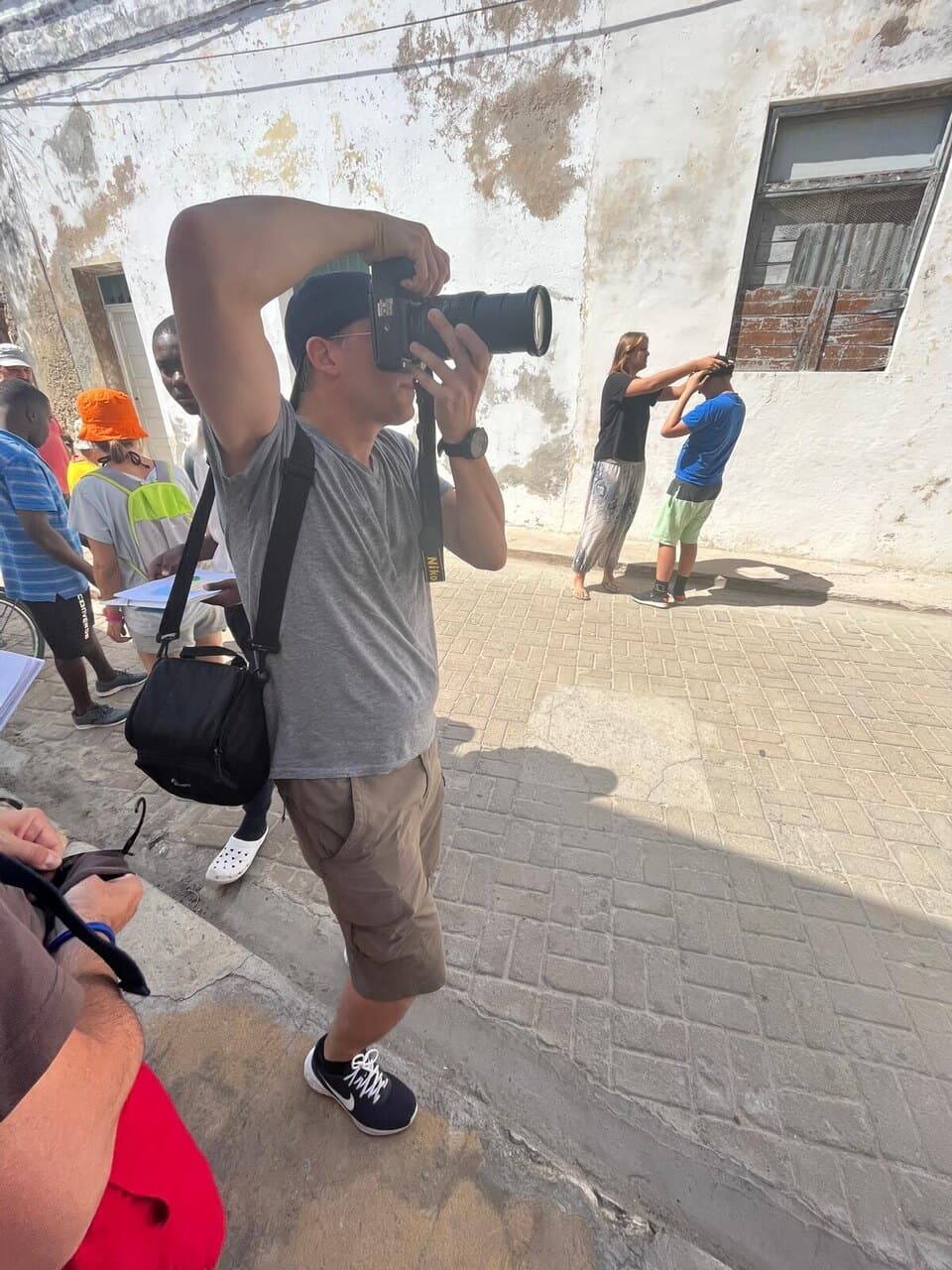 One of us lining up a shot with a big camera in a street of old, sun-bleached walls