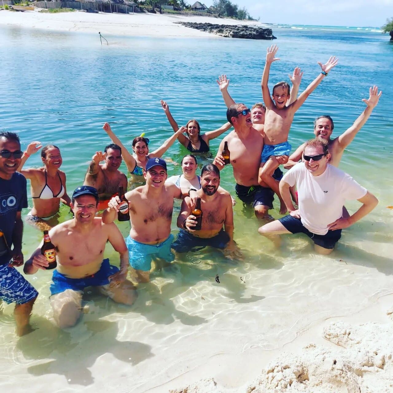 A crowd of us waist-deep in clear water, arms in the air