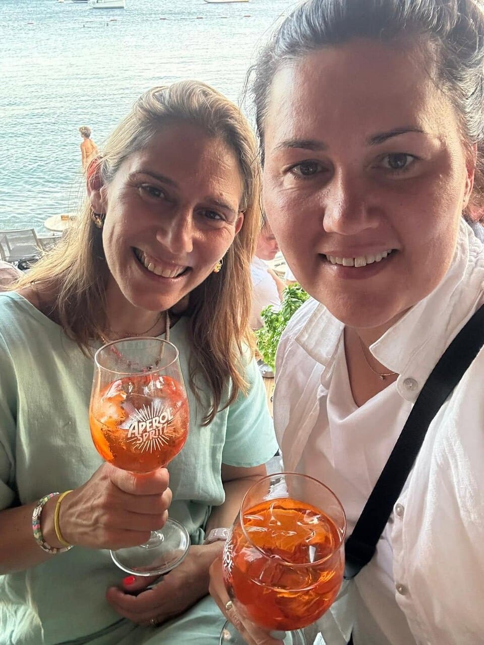 Two of us raising Aperol spritzes by the sea