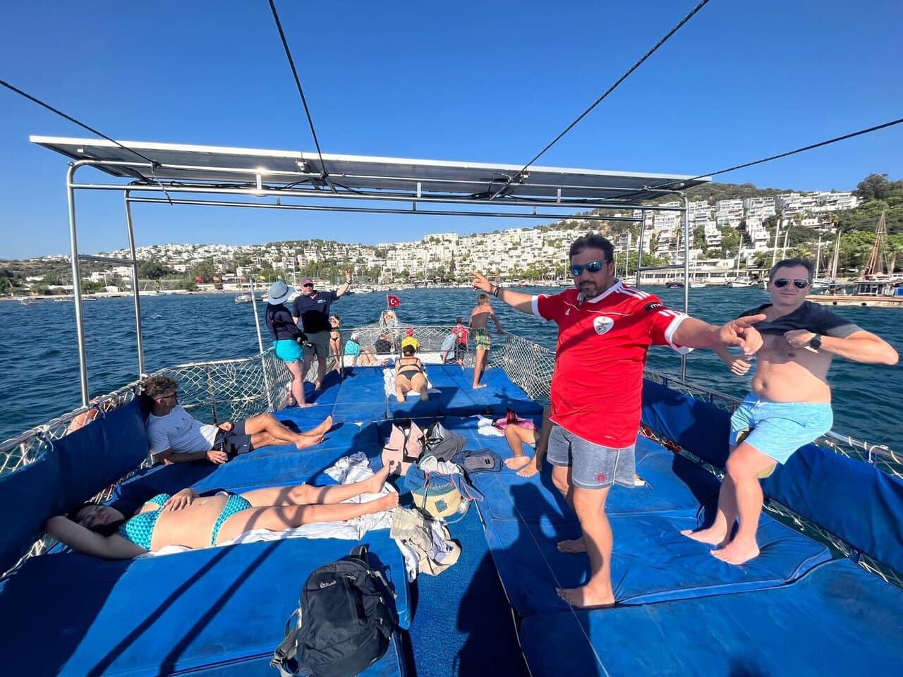 Two of us dancing on the deck of a boat while others sunbathe, a white town on the hills behind