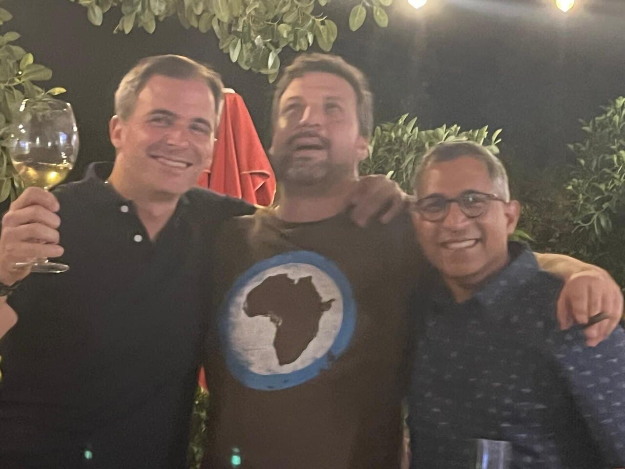 Three of us arm in arm under a tree at night, one raising a glass of white wine