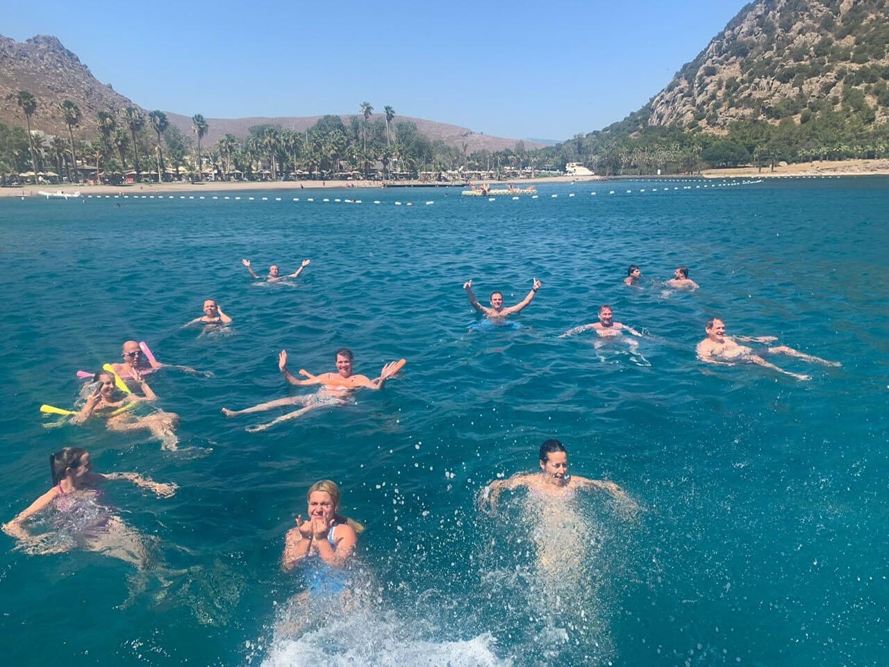 A dozen of us swimming off the boat in a turquoise bay, with mountains behind