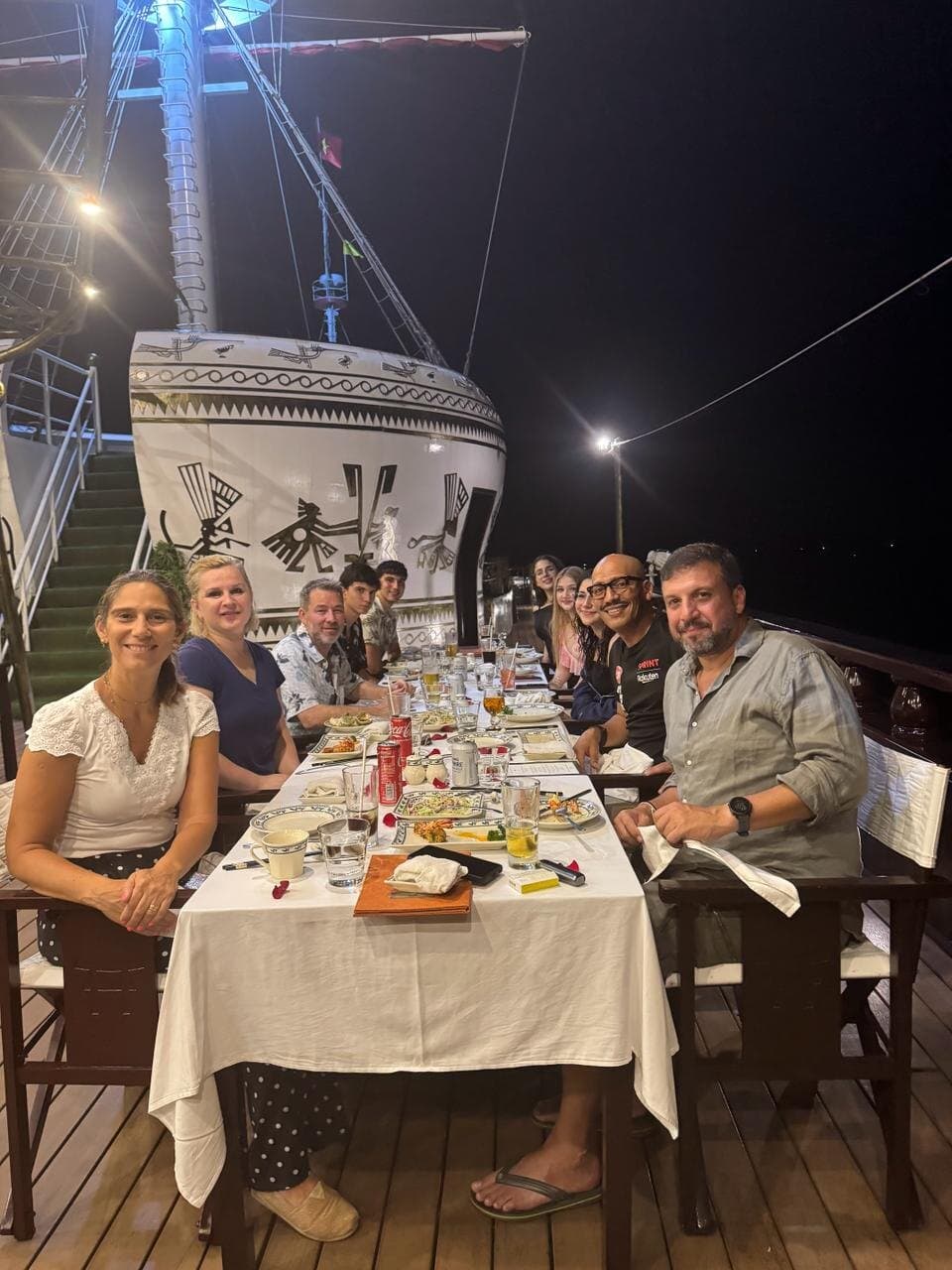 Dinner at a long table on the deck of a boat at night